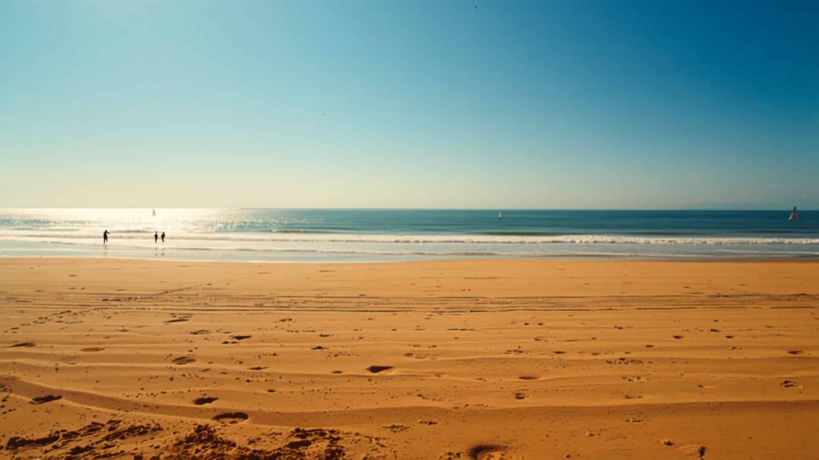 Côte vendéenne au coucher du soleil : plage de sable, vagues et voiliers sur l'océan Atlantique